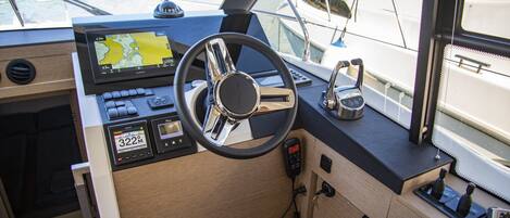 A boat's control station with a steering wheel, navigation screen, and various control buttons.
