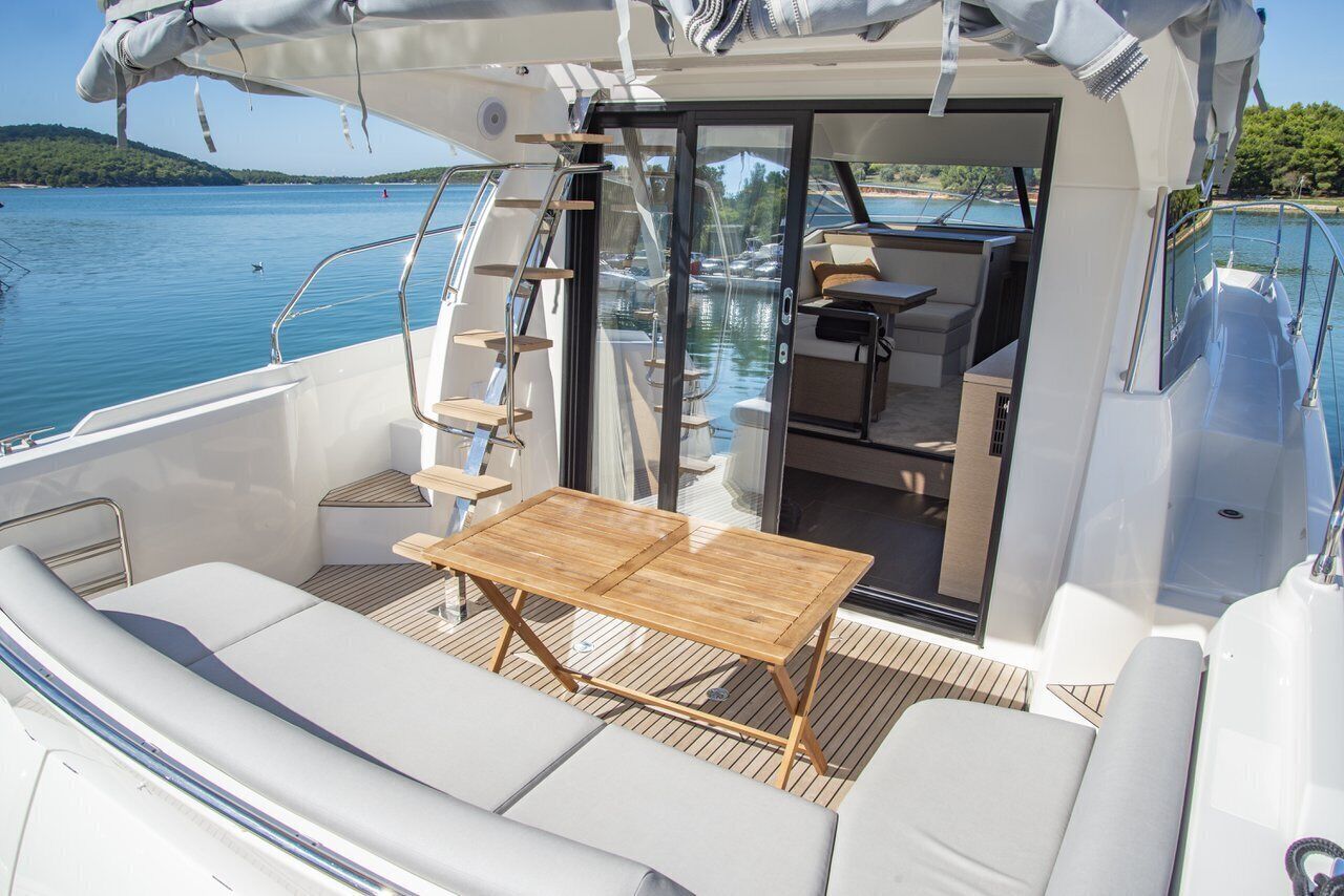 A yacht's deck with a wooden table, cushioned seating, and a glass door leading to an interior space.