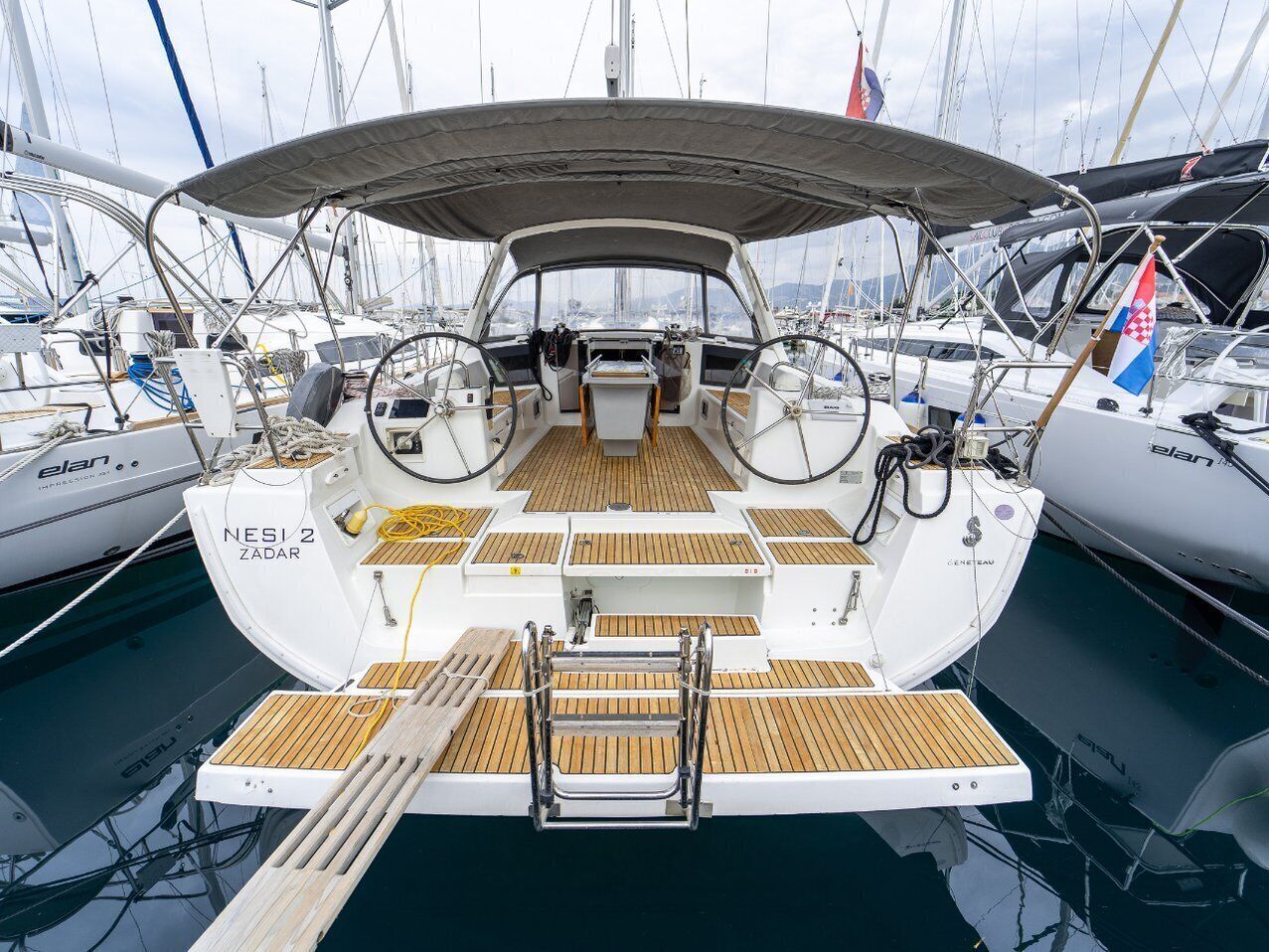 A sailboat docked at a marina with a covered deck, wooden flooring, and a flag.