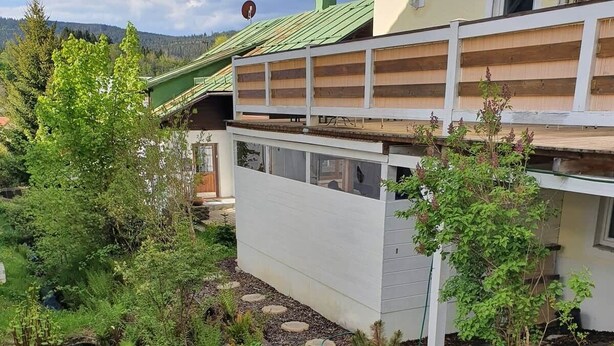 Ett modernt hus med ett grönt tak, en liten bäck och frodig grönska.