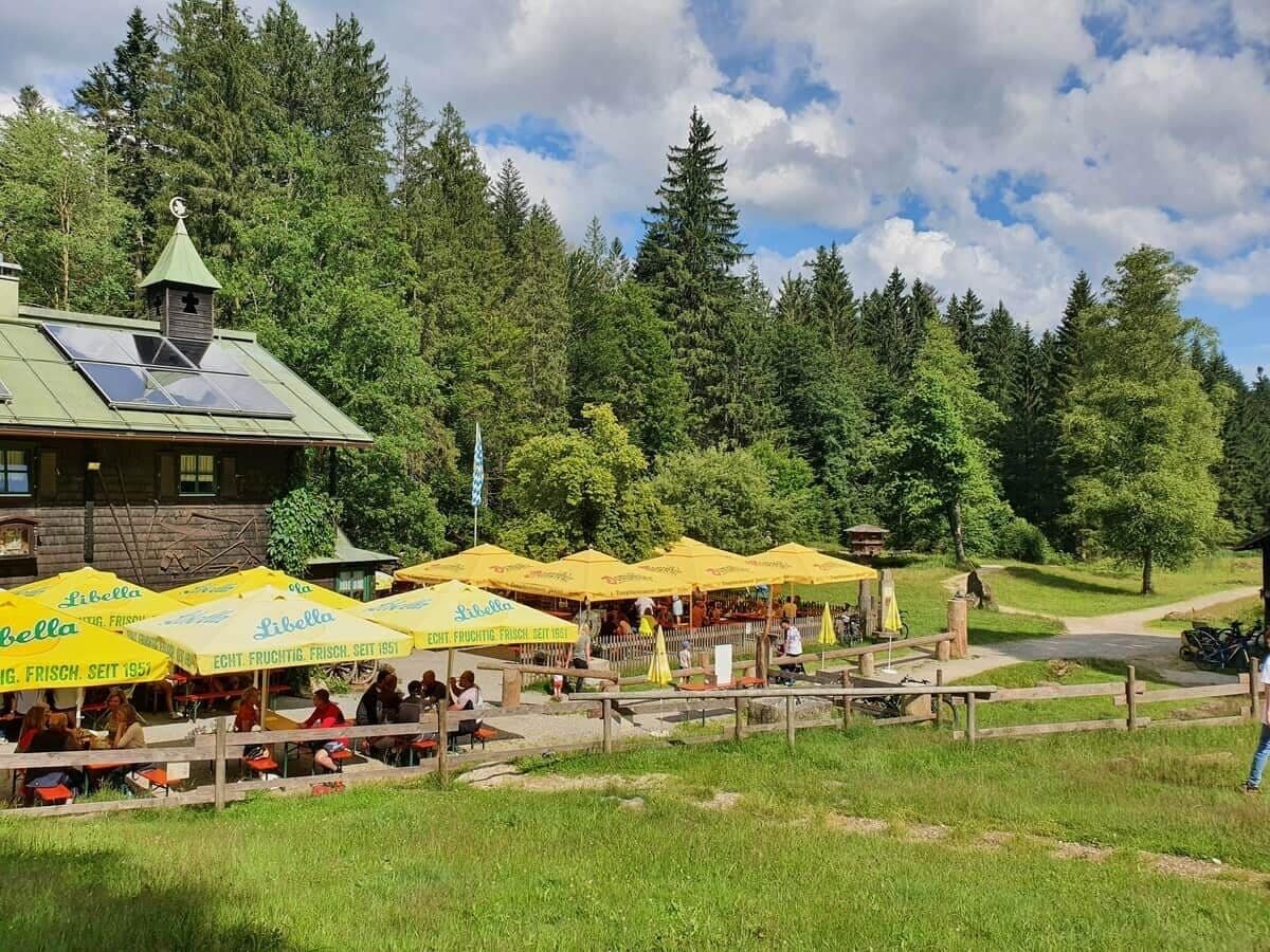 Ein rustikaler Essbereich im Freien mit gelben Sonnenschirmen, Holztischen und einer Bergkulisse.