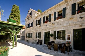 A stone building with multiple windows, some with shutters, and a covered outdoor seating area with benches and a table. - Sun-Kissed Sailing Adventure in Zadar, Croatia (Bibinje)