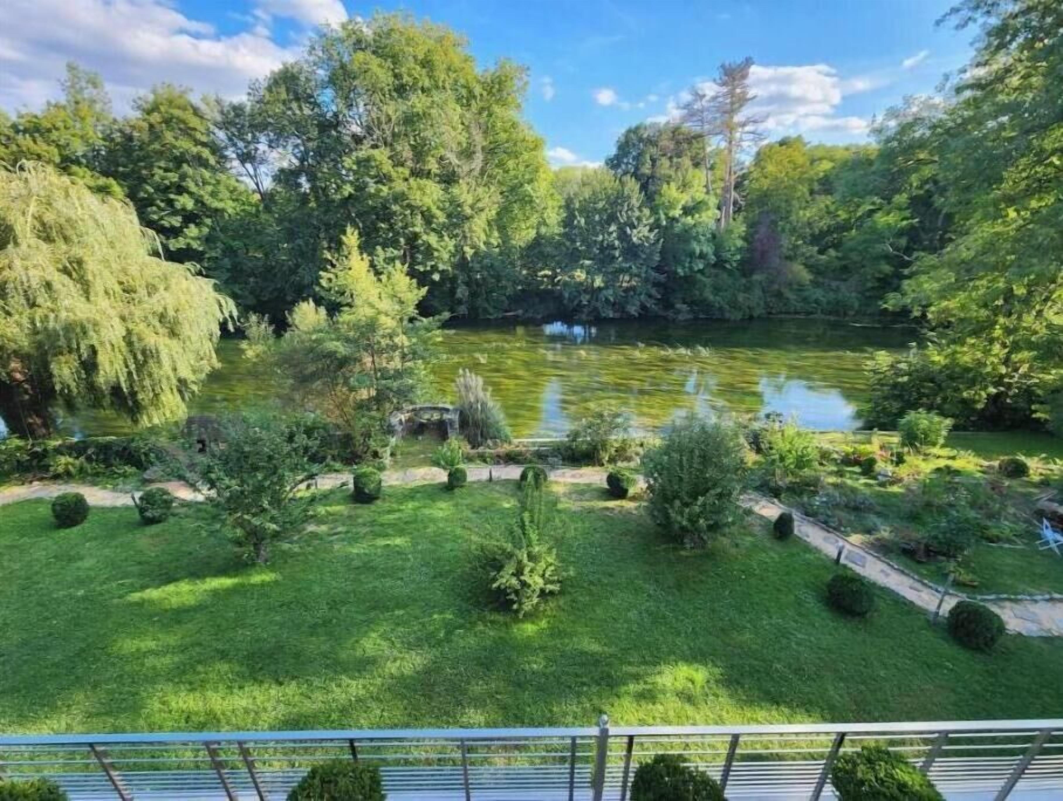 Un jardin luxuriant avec un étang, entouré de différents arbres et arbustes.