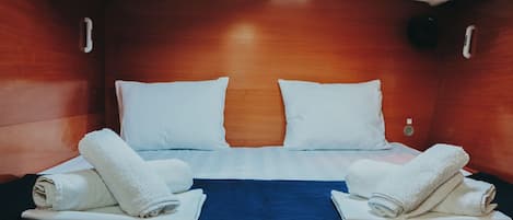 Cama de casal com lençóis brancos, duas toalhas, cabeceira de madeira e colcha azul escura.