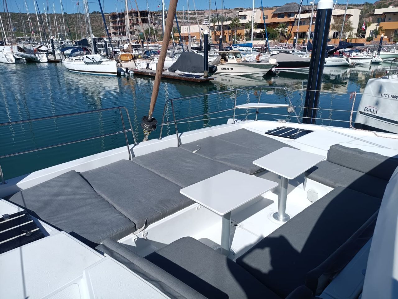 Uma marina com barcos atracados, uma área coberta com assentos e mesas, e edifícios ao fundo.