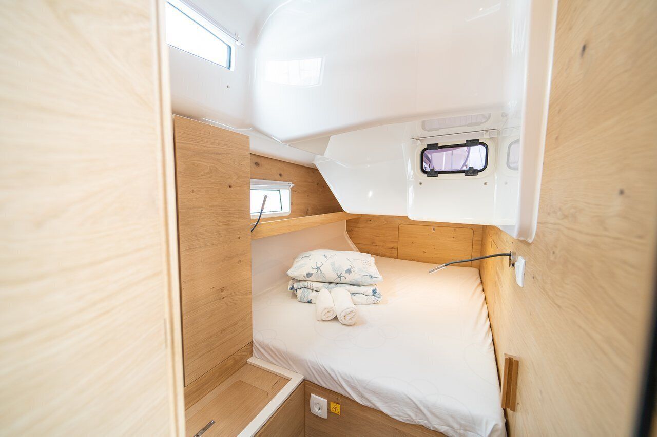 Interior compacto de una caravana con una cama individual, una ventana pequeña y un enchufe.