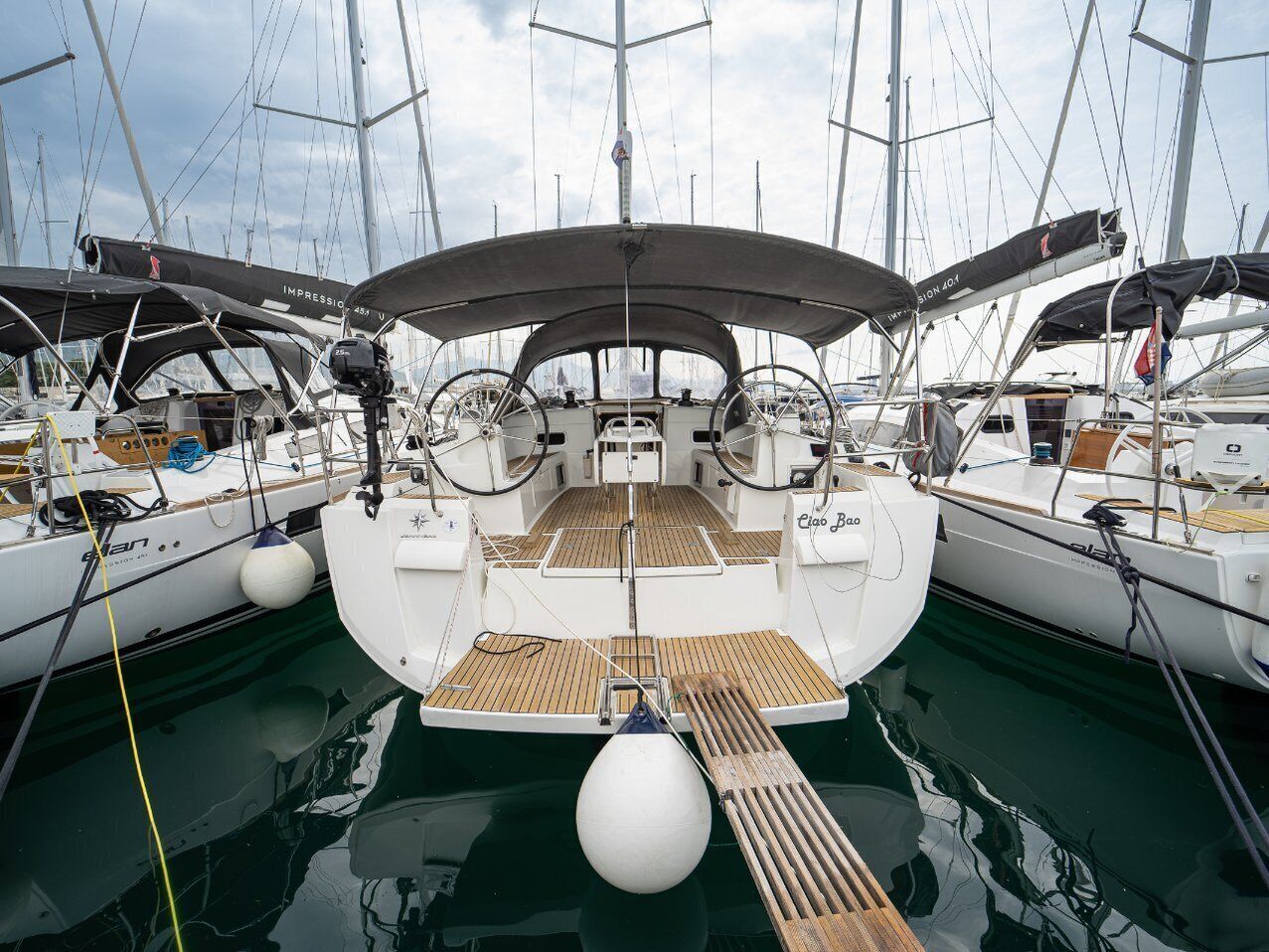 Marina con varios veleros amarrados, destacando cubiertas de madera y cascos blancos.