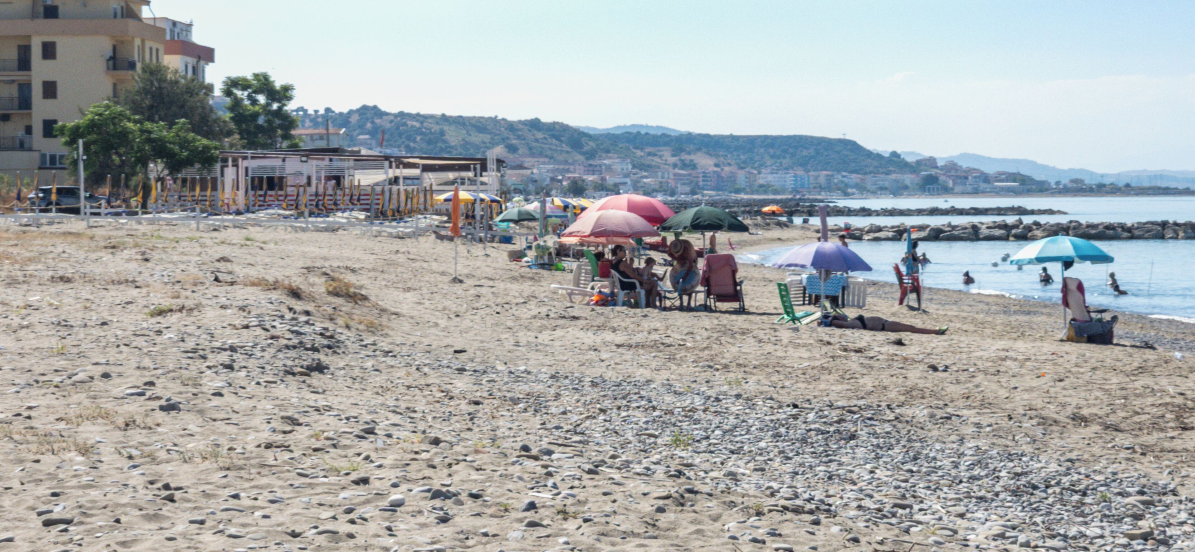 A beach with umbrellas, chairs, and a rocky shoreline.