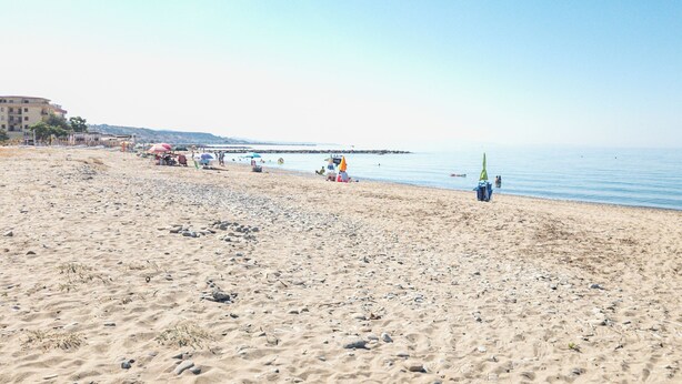 Una playa con arena, sombrillas y algunas personas.