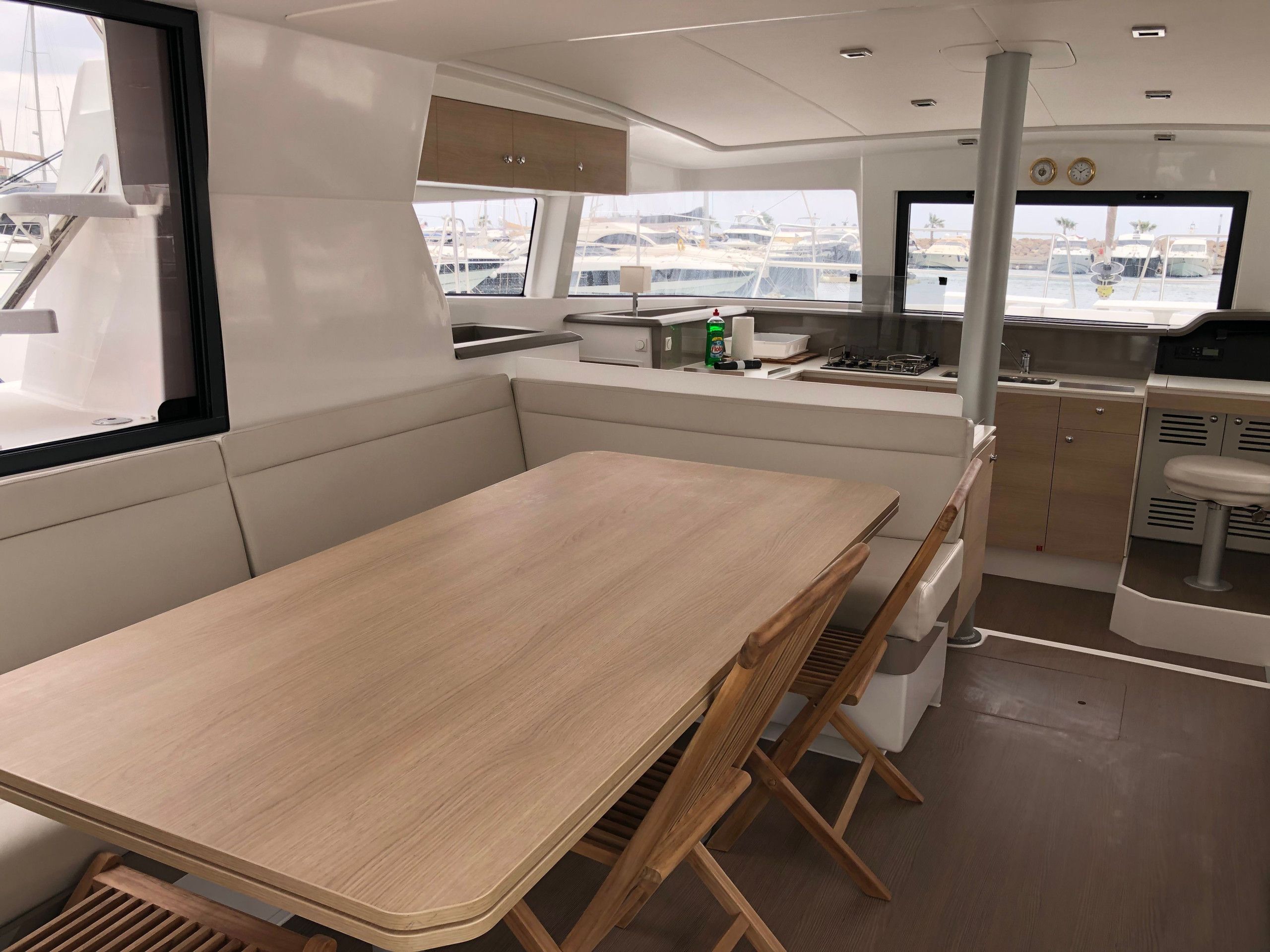 A compact galley with a wooden table and seating, a small kitchenette, and a view of the marina through the windows.