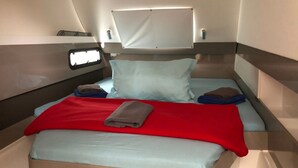 A compact bed with a red blanket, two pillows, and a window above.