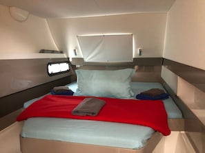 Een klein bed met een rode deken, twee kussens, en een raam erboven.