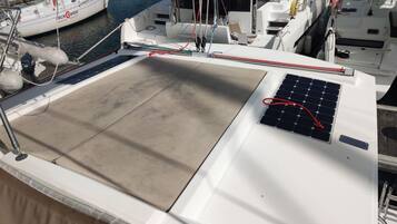 Un pont de bateau équipé d’un panneau solaire, une cabine blanche et une voie navigable où d’autres bateaux circulent.