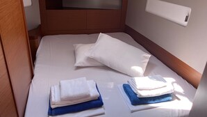 Een net opgemaakt bed met witte lakens, een houten hoofdbord en een klein nachtkastje met een witte lamp.
