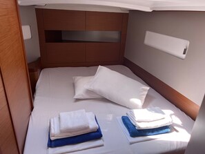 A neatly made bed with white linens, a wooden headboard, and a small bedside table with a white lamp. - Sun-Kissed Sailing Adventure in the Stunning Sporades Islands (Loutraki)