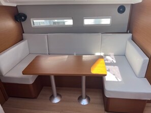 A compact seating area with a table, cushioned benches, and a small fan. - Sun-Kissed Sailing Adventure in the Stunning Sporades Islands (Loutraki)