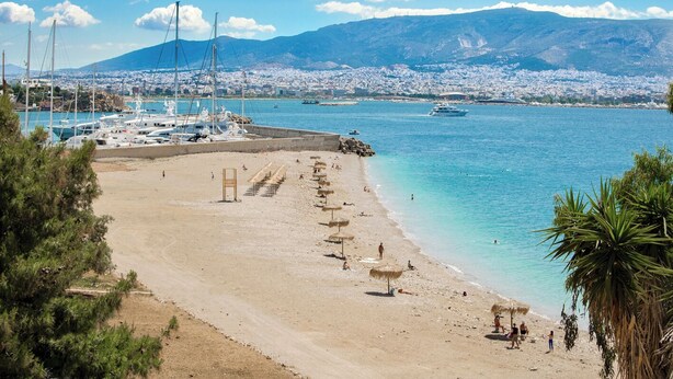 Une plage avec des parasols, une marina avec des bateaux, et un paysage urbain en arrière-plan.