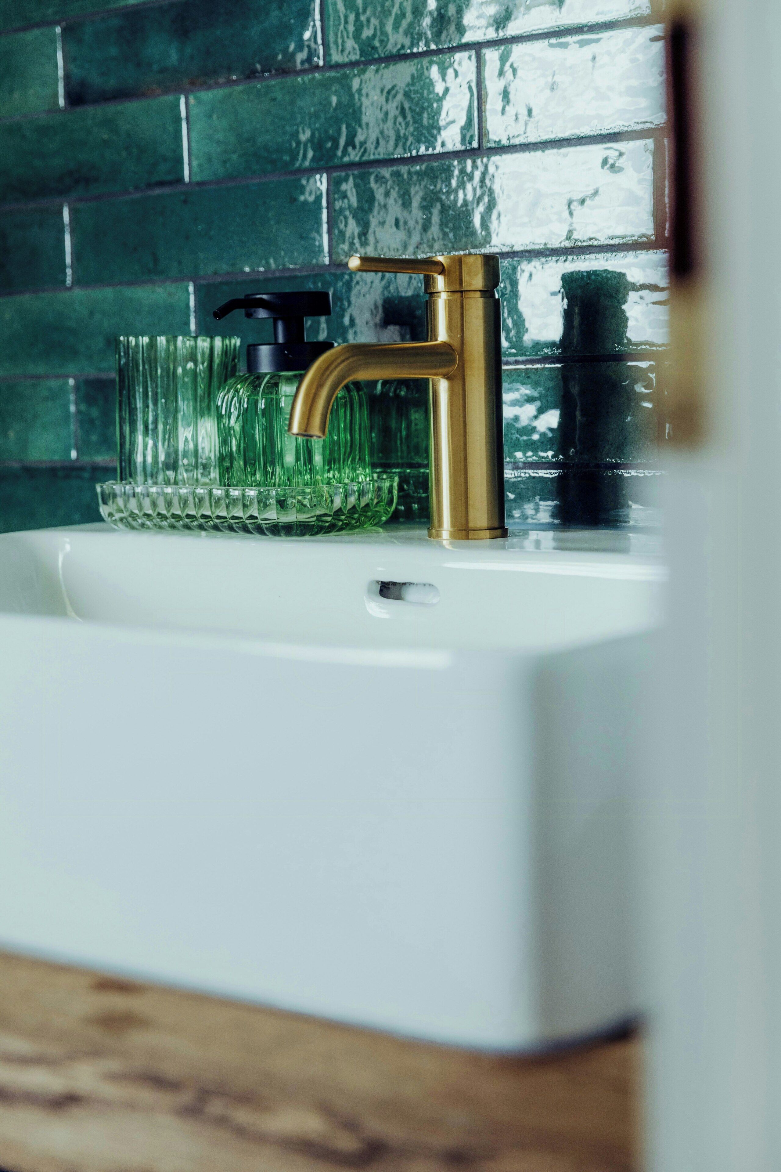 Een witte wastafel met een gouden kraan en een groene glazen zeepdispenser.