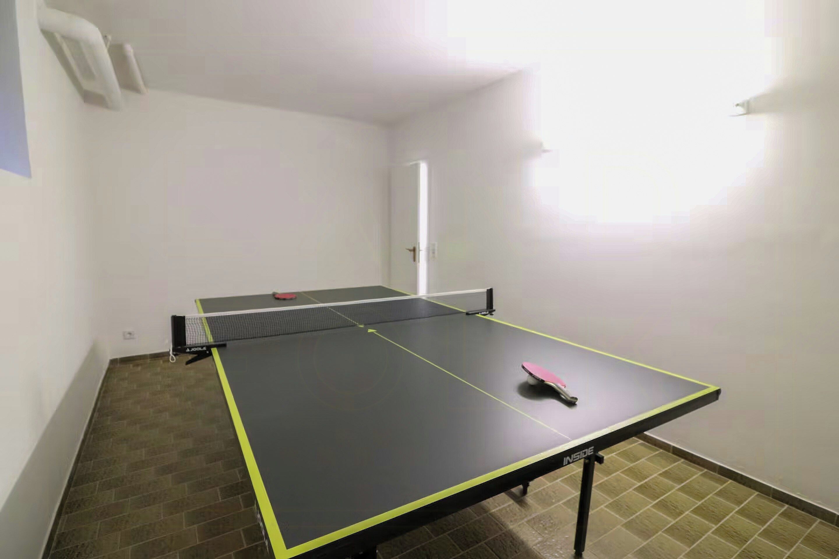 A ping pong table with a net in a room with tiled flooring and white walls.