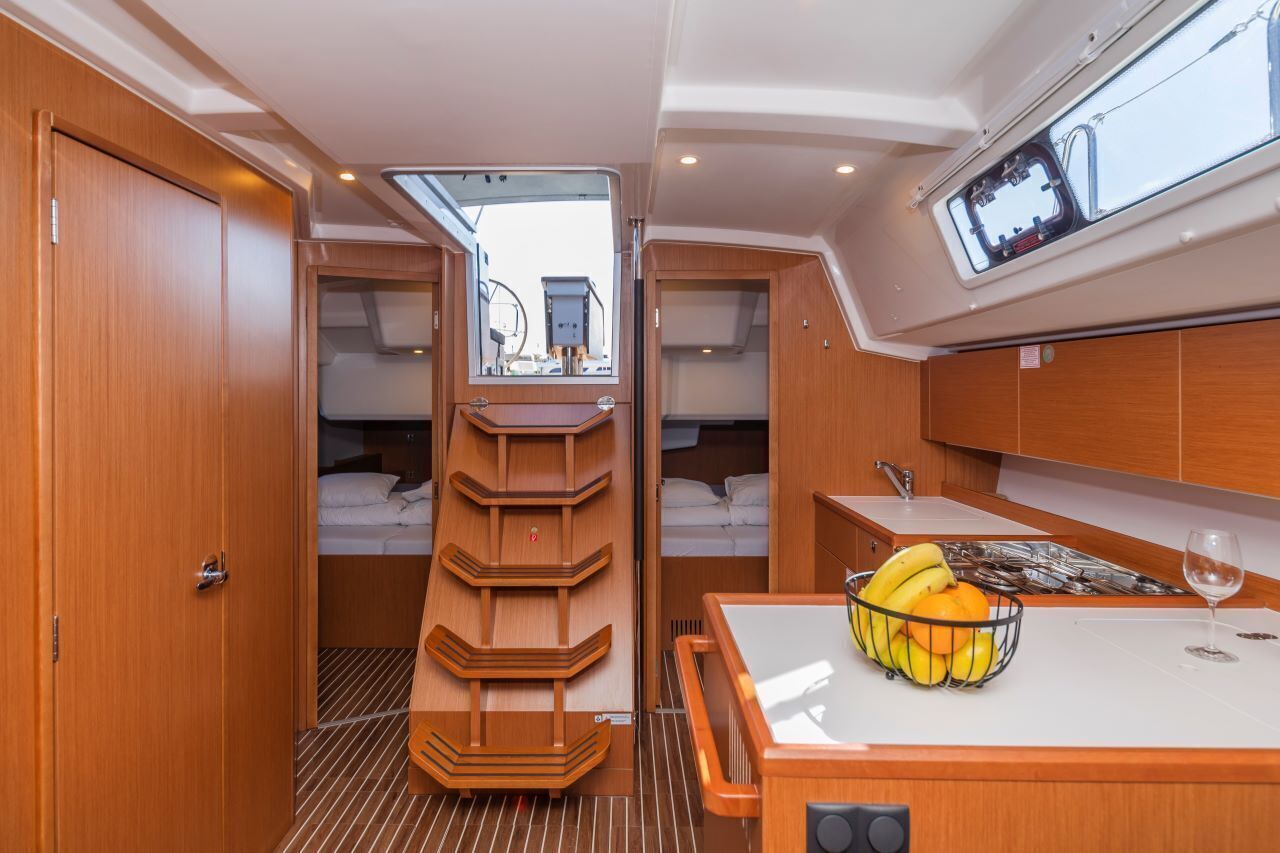 A compact galley with a central wooden shelf, a small table with a fruit bowl, and a window above the sink.