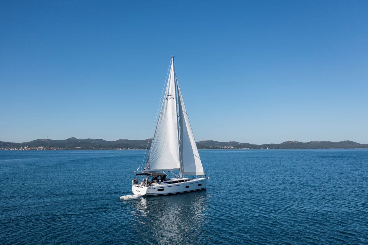 A sailboat on calm waters with a clear sky and distant mountains.