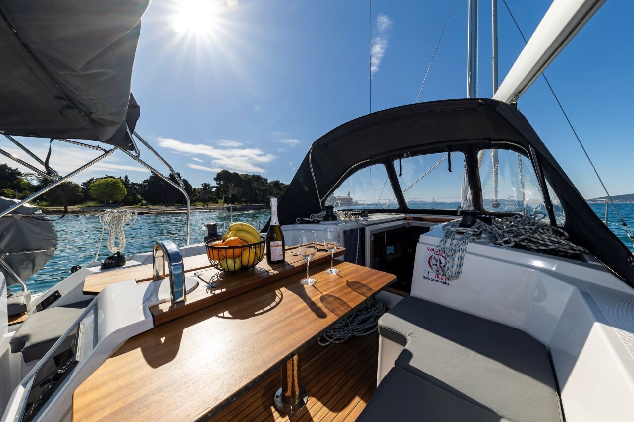 A boat deck with a wooden table, a bowl of fruit, a bottle of wine, and a small bar area.