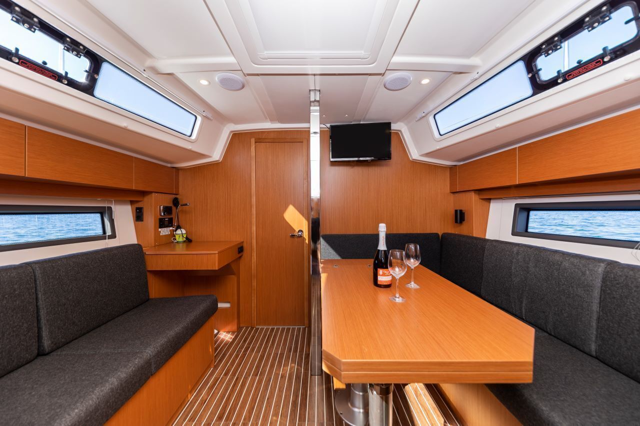 A compact interior with a central table, cushioned seating, a television, and windows.