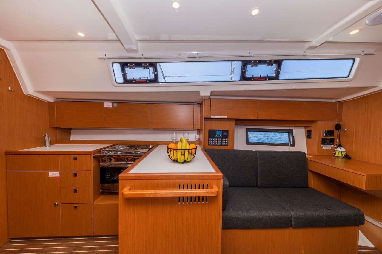 A compact galley with a stove, a small sink, and a seating area with a control panel and a screen.