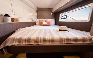Une chambre à coucher compacte et bien éclairée, avec un lit, des oreillers, un chapeau et une fenêtre donnant sur un quai.