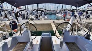 A boat deck with a steering wheel, a small seating area, and a view of other boats in the marina. - Sun-Kissed Sailing Adventure in Zadar, Croatia (Bibinje)