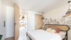 Ein Schlafzimmer mit Bett, einer Tür zu einem Balkon und einer Wand mit tropischem Wandpapier.