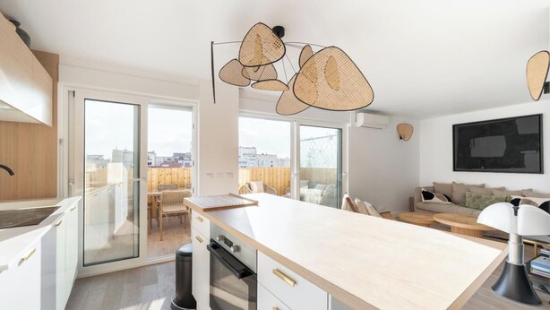 Eine moderne Küche mit einer großen Kochinsel, Schiebeglasfenstern zu einem Balkon und einem wandmontierten Flachbildfernseher.