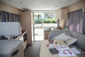 Interior compacto de uma RV com uma cama, uma pequena mesa com desenhos infantis, uma TV e uma cozinha compacta.
