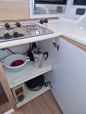 A kitchen with a gas stove, a coffee maker, a colander, and a Nespresso machine.