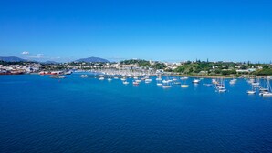 Une ville côtière dotée d’un port de plaisance rempli de bateaux, d’un ciel bleu azur et d’un paysage vallonné en arrière-plan.
