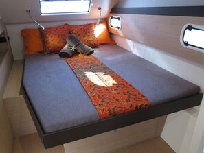 Uma cama compacta com colcha estampada, duas almofadas e uma pequena janela sobre a cama.
