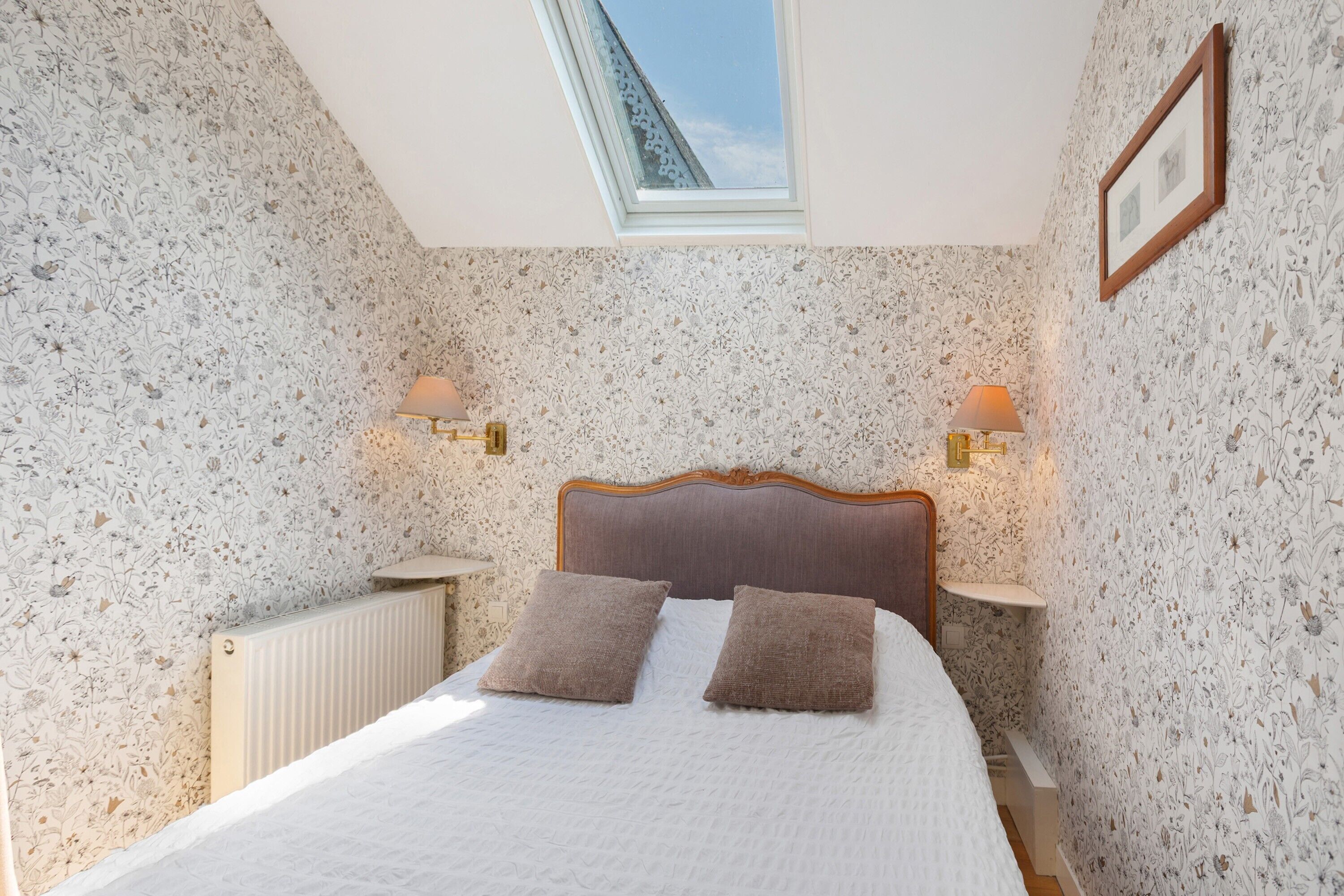 Ein Schlafzimmer mit Oberlicht, zwei Nachttischlampen, einem Holzkopfende und einer Heizung.
