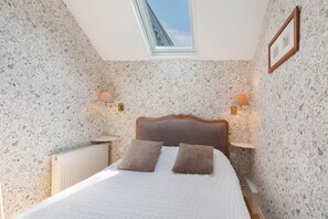 A bedroom with a skylight, two bedside lamps, a wooden headboard, and a radiator.