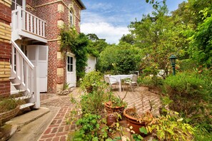 Casa de ladrillo con una escalera blanca y un jardín con plantas en macetas y una mesa.