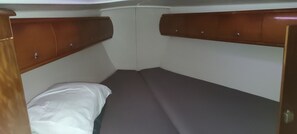 Une petite pièce fermée, avec un lit simple, une tête de lit en bois et un oreiller blanc.