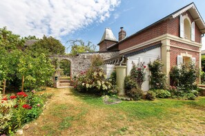 A brick house with a garden, a stone archway, and a clear sky.