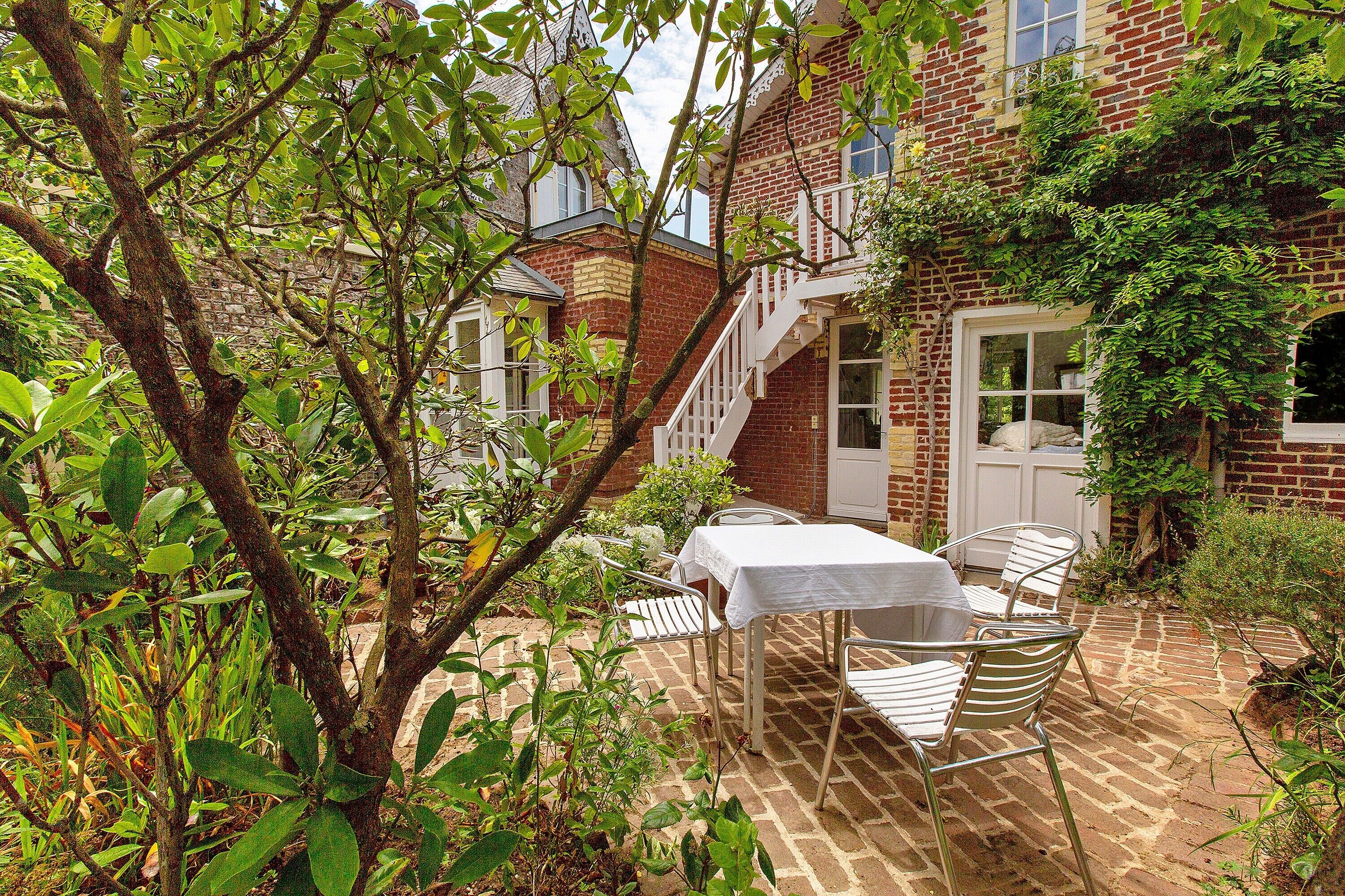 Une maison en briques avec une porte blanche, un escalier et une table avec des chaises à l’extérieur.