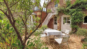 A brick house with a white door, a staircase, and a table with chairs outside.