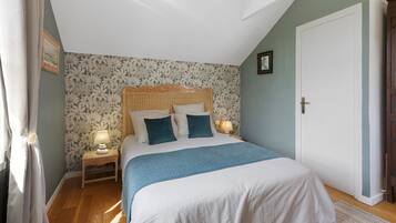 Een slaapkamer met een bed, twee bedlampjes, een nachtkastje, een deur en een raam met gordijnen.