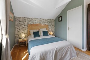 A bedroom with a bed, two bedside lamps, a nightstand, a door, and a window with curtains.