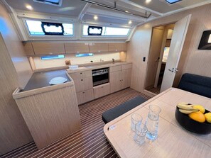 A compact kitchen with a dining area, a small oven, and a table with glasses and fruit. - Sun-Kissed Sailing Adventure in Istria, Croatia (Pula)