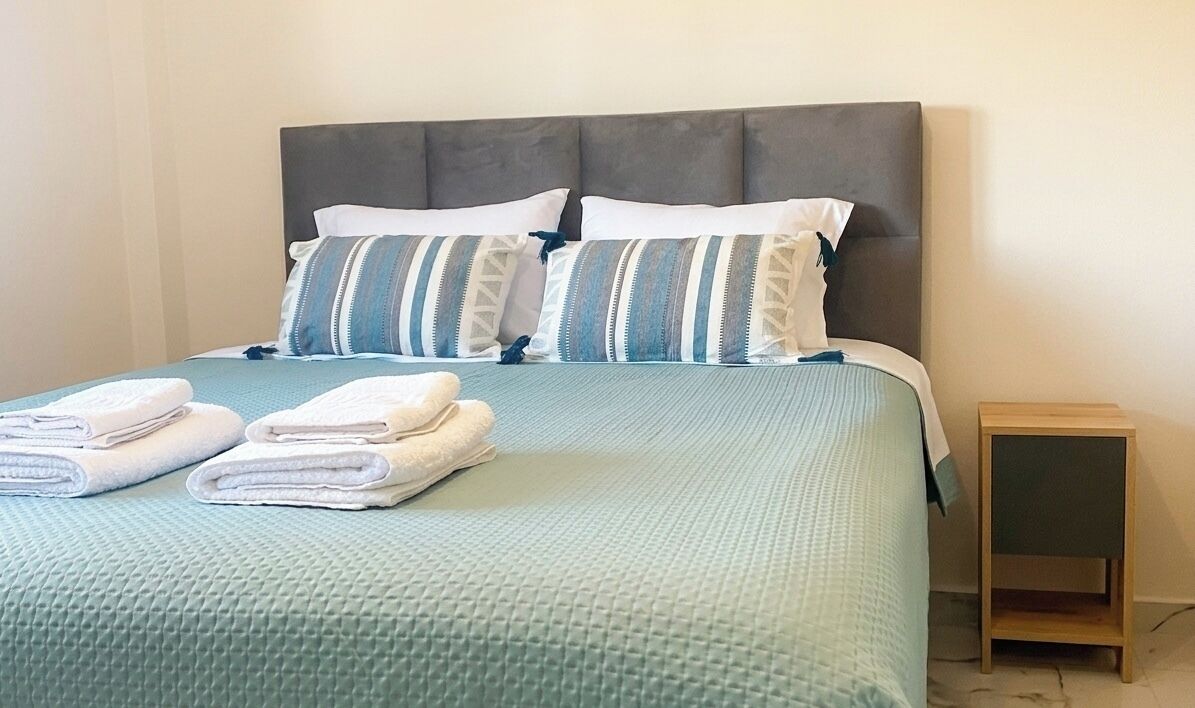 A bed with a grey headboard, two pillows, and folded towels.