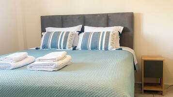 A bed with a grey headboard, two pillows, and folded towels.