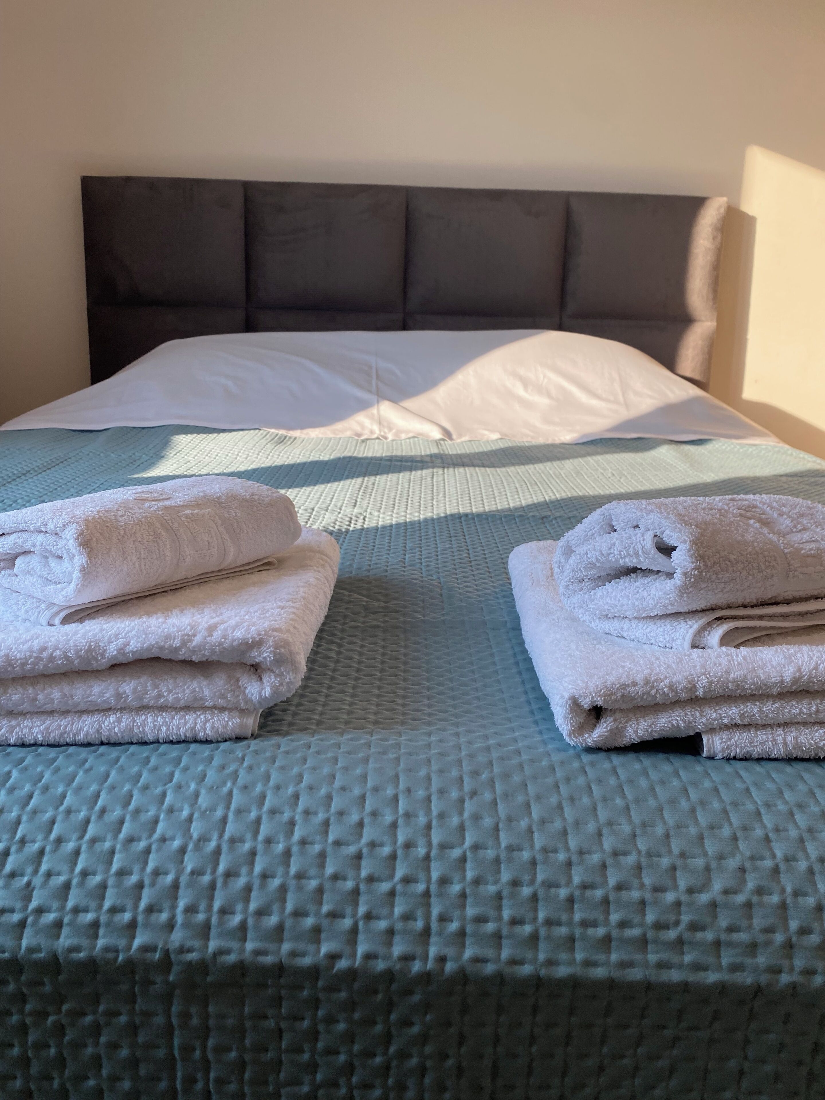 Una cama bien hecha con colcha acolchada, almohadas y toallas dobladas.