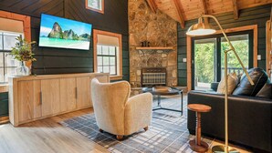 Un salon chaleureux avec une cheminée en pierre, un téléviseur fixé au mur, un canapé confortable et un plafond en bois.